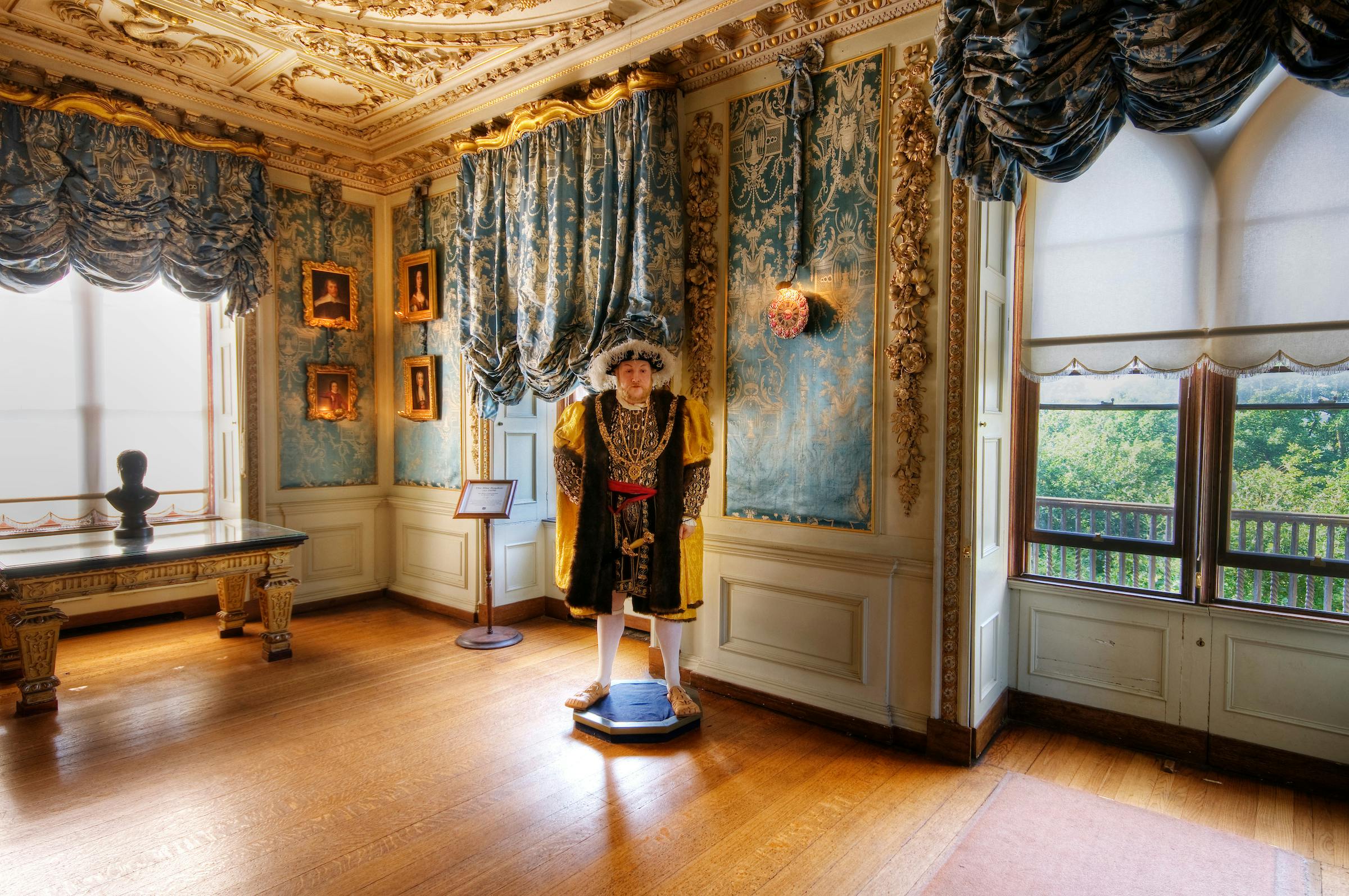 A lavishly decorated room with ornate walls, rich curtains, and a life-sized historical figure's statue in period clothing.