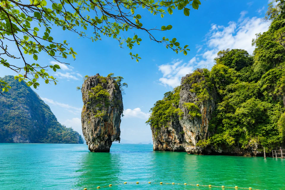 A scenic view of limestone islands with green vegetation in clear turquoise water under a blue sky, framed by tree branches.