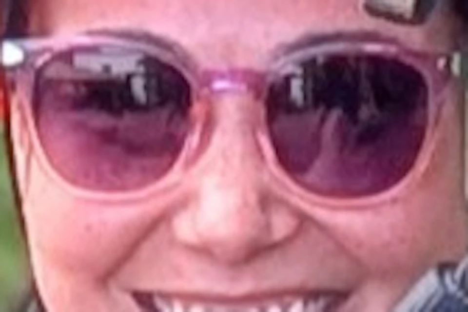 A person ziplining through a forest, wearing a helmet, harness, and sunglasses, smiling at the camera.