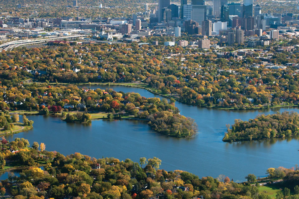 Aerial view of a cityscape with lakes surrounded by colorful autumn trees and urban buildings in the background.