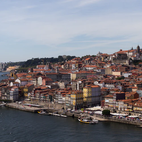 En naturskön utsikt över en stad vid floden med färgglada byggnader, en avlägsen bro och båtar på vattnet.