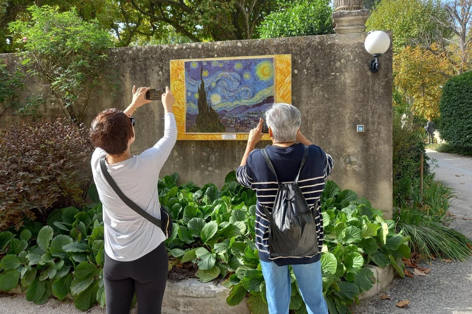 Two people seen from behind taking a photo of a plaque with a painting by Vincent Van Gogh