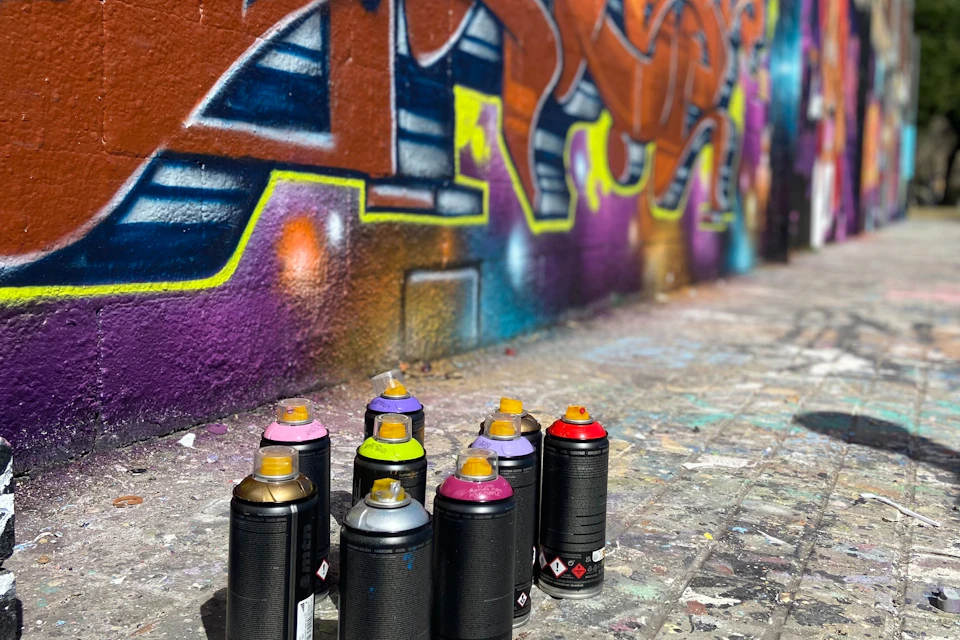 Colourful spray cans in front of an even more colourful mural in Barcelona