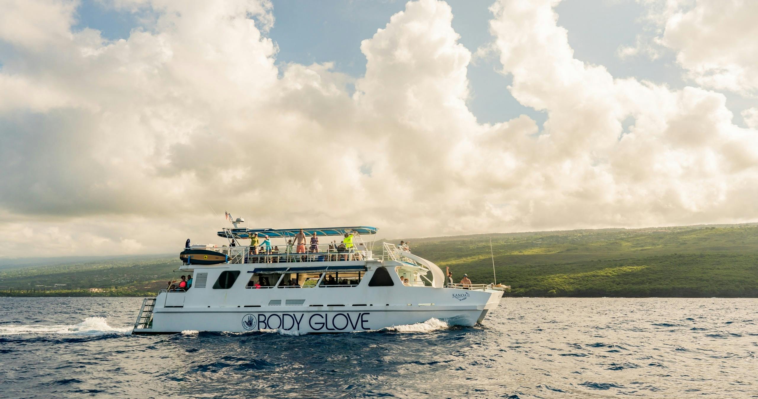 A boat labeled 'Body Glove' on a calm sea, with people visible on deck, under a partly cloudy sky and distant land.