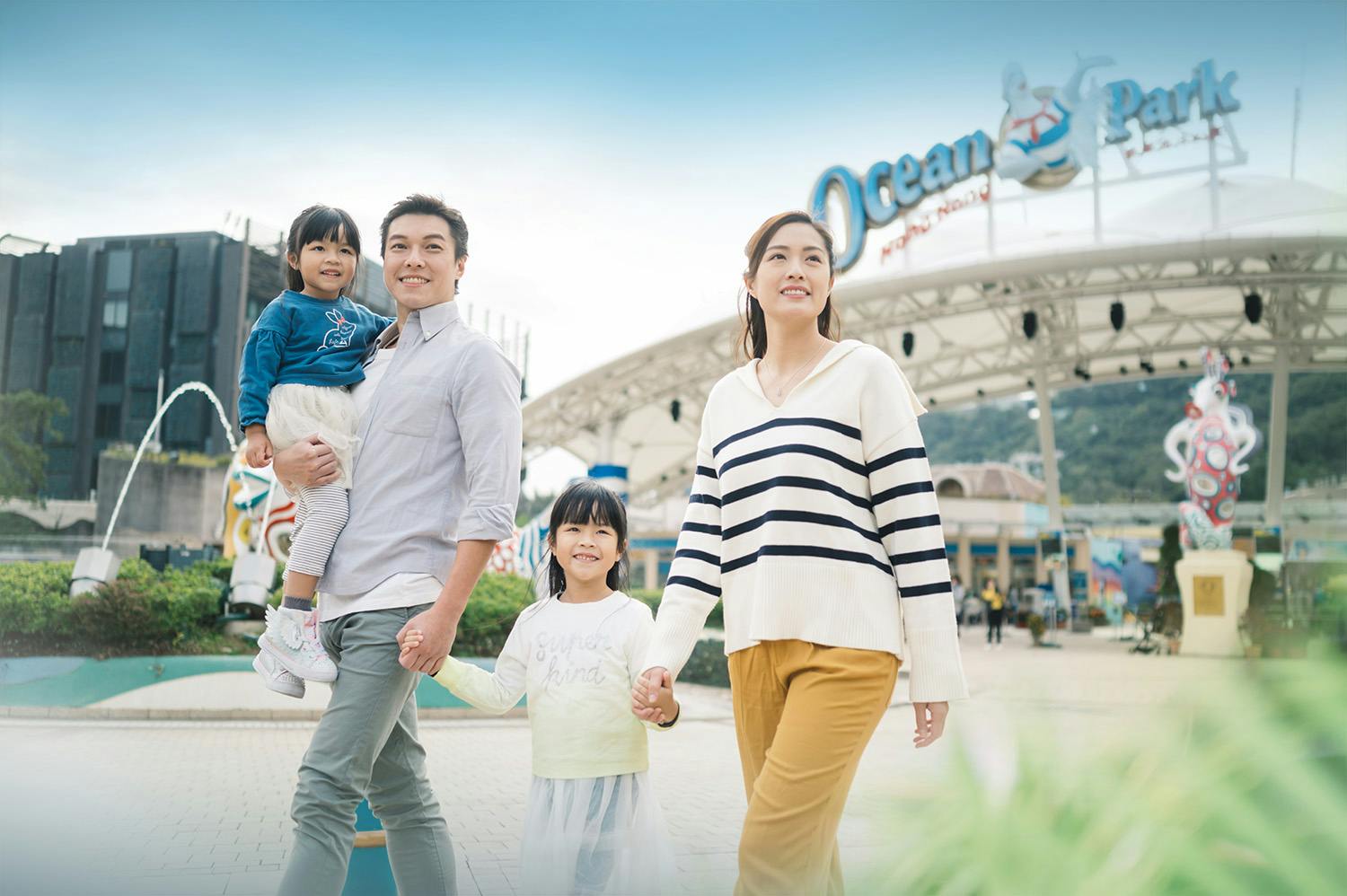 A family of four smiling and walking outdoors near an amusement park entrance labeled "Ocean."