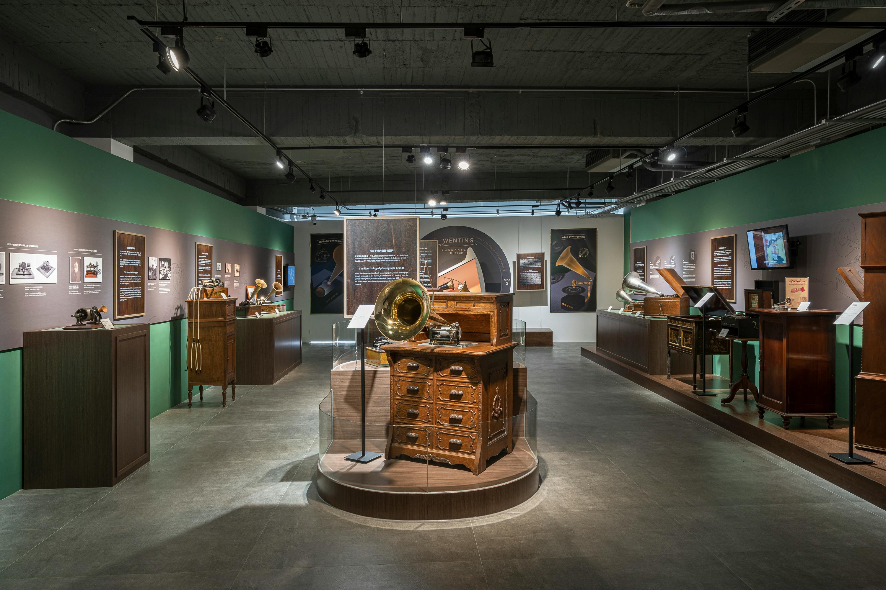 A museum exhibit featuring vintage gramophones and cabinets, displayed in a well-lit room with informational panels on the walls.