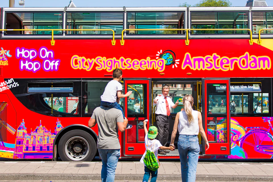 A family boards a red double-decker bus labeled "City Sightseeing Amsterdam," with the driver welcoming them.