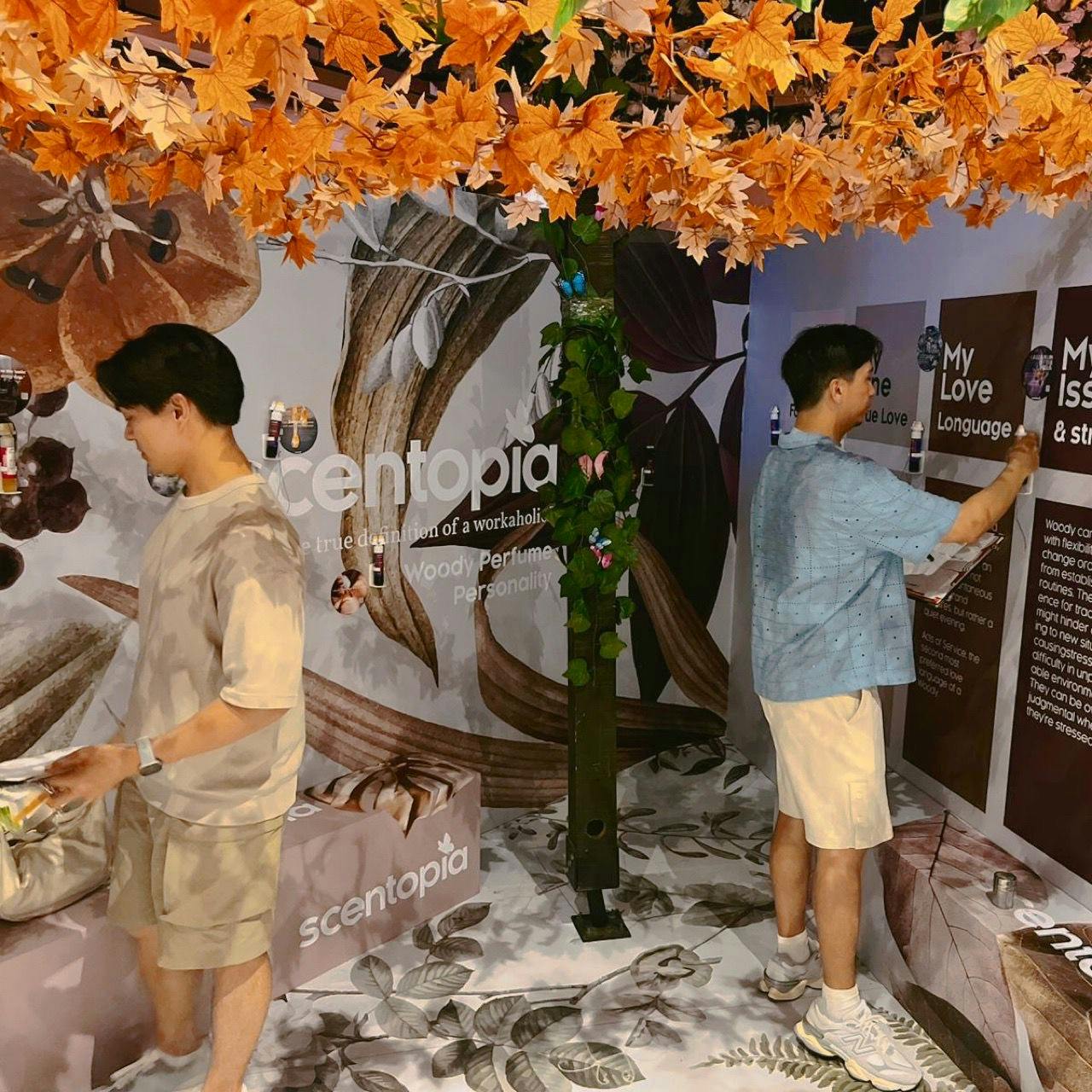 Two people interact with displays in an autumn-themed exhibition booth. The wall reads "scentopia" with images of spices.