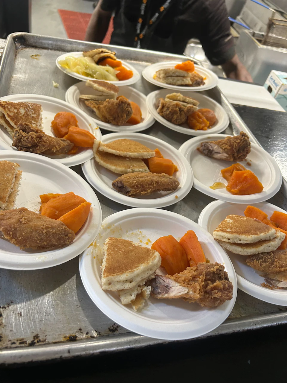 Plates of food with fried chicken, pancakes, and sweet potatoes on a metal surface.