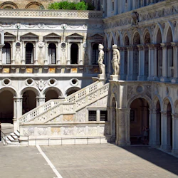 Utsmyckad marmorgård med välvda fönster, statyer och en stor trappa. En person står nära en ingång till vänster.