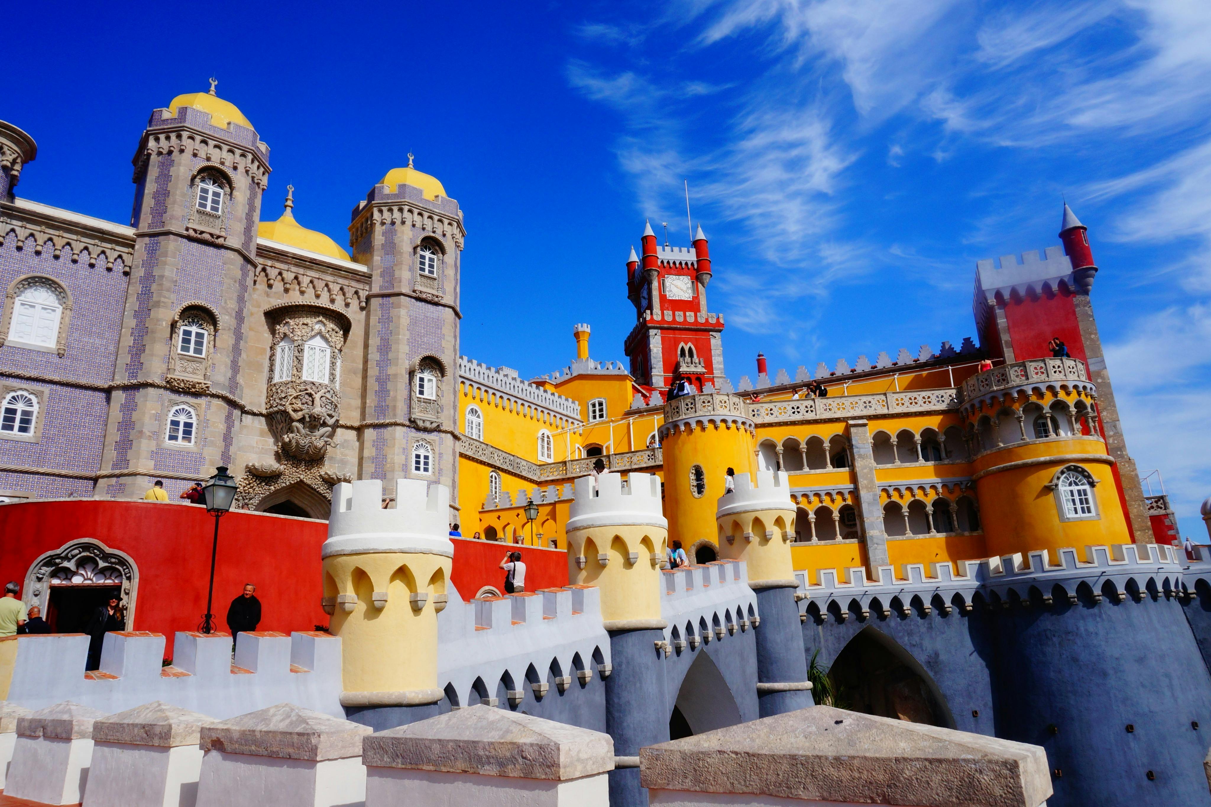 Un castello dai colori vivaci con torri gialle, rosse e grigie sotto un cielo blu brillante, caratterizzato da intricati dettagli architettonici.