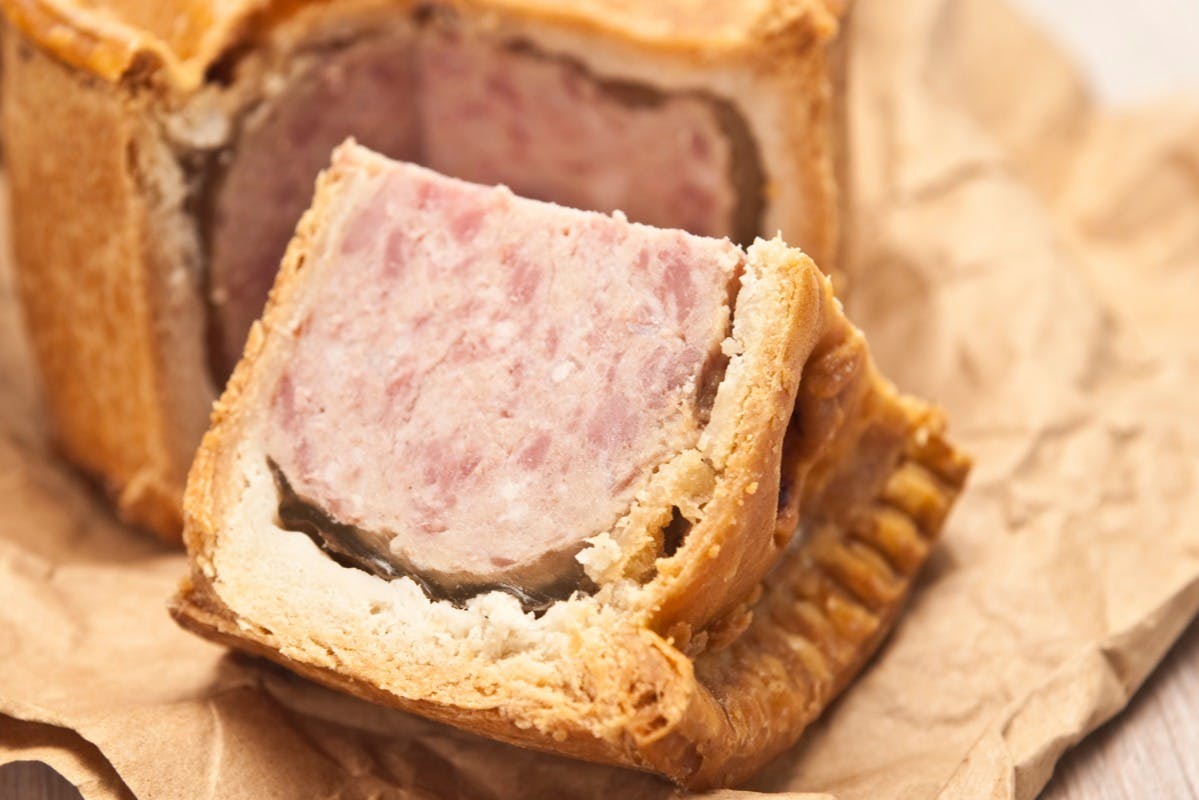 Ένα κοντινό πλάνο μιας χοιρινής πίτας σε φέτες με χρυσή κρούστα και ροζ γέμιση κρέατος σε καφέ λαδόκολλα.