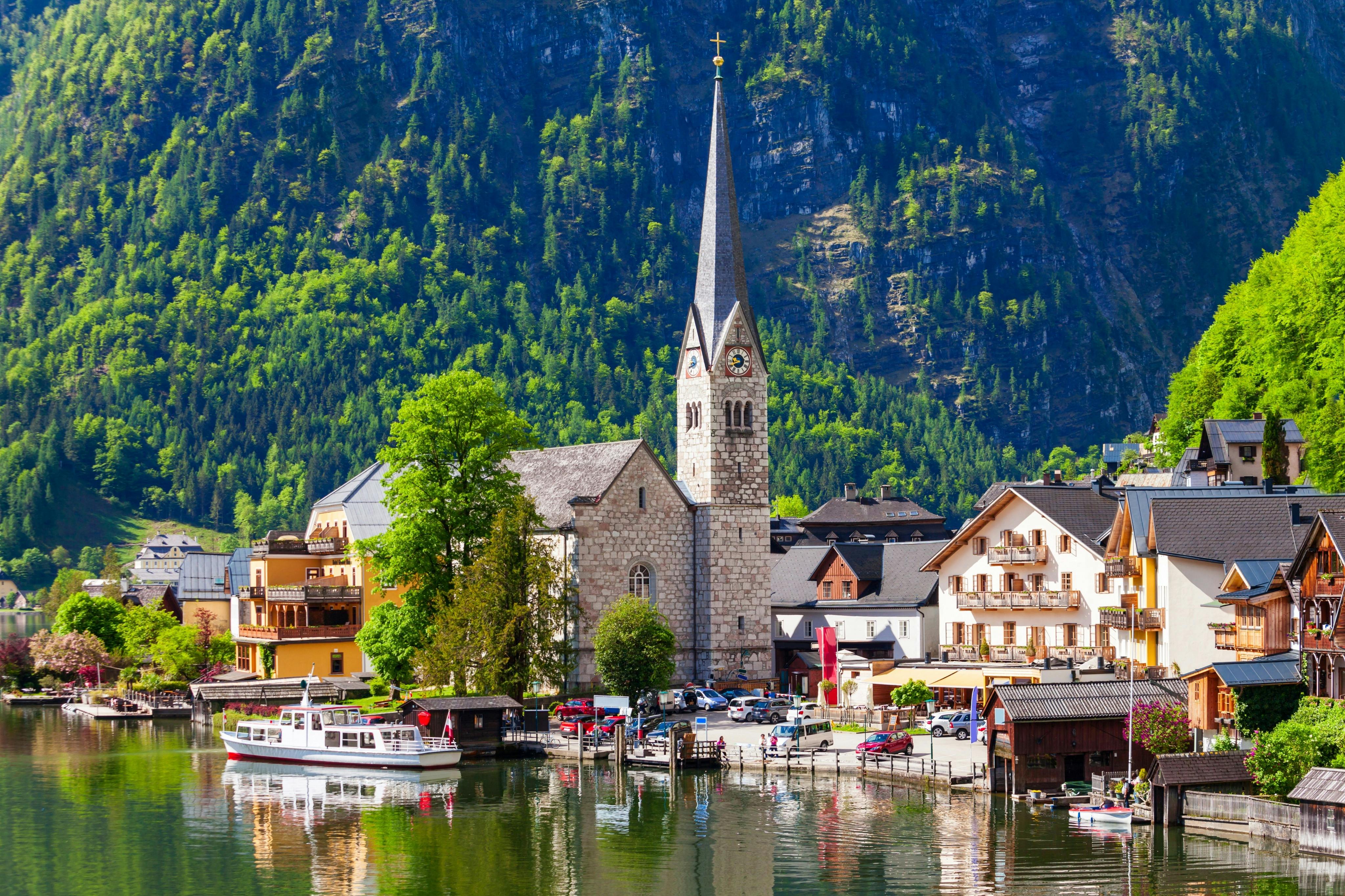Un village au bord du lac avec une église et un clocher proéminents, des bâtiments charmants et des montagnes verdoyantes en arrière-plan.