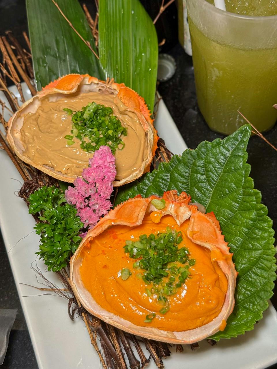 Two crab shells filled with creamy seafood mixture, garnished with green onion and served with leaves and flowers on a plate.
