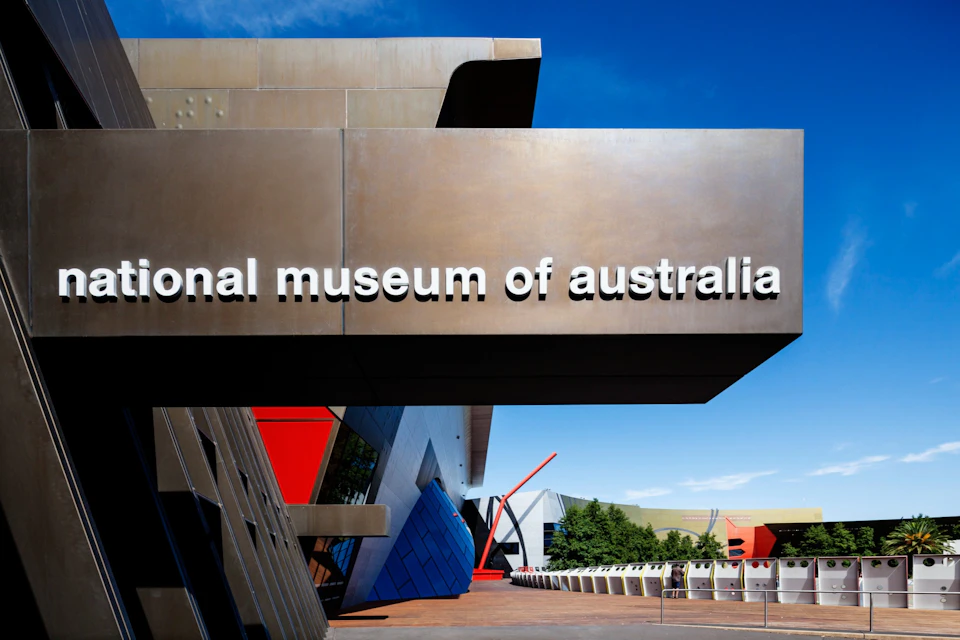 The exterior of the National Museum of Australia featuring bold architectural shapes and signage under a clear blue sky.
