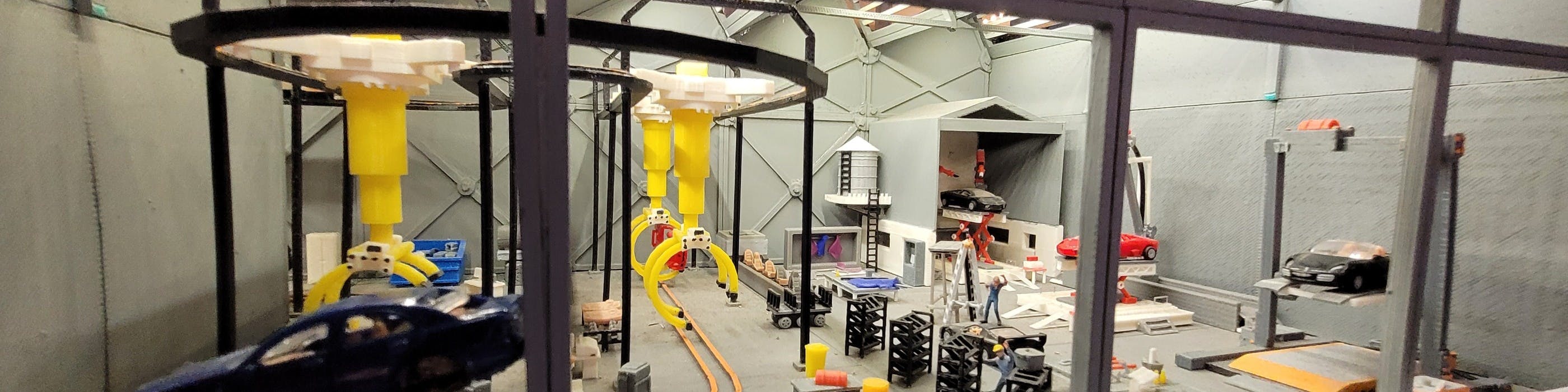 Una maqueta detallada que representa una escena industrial con brazos robóticos amarillos, un silo y diversos equipos.