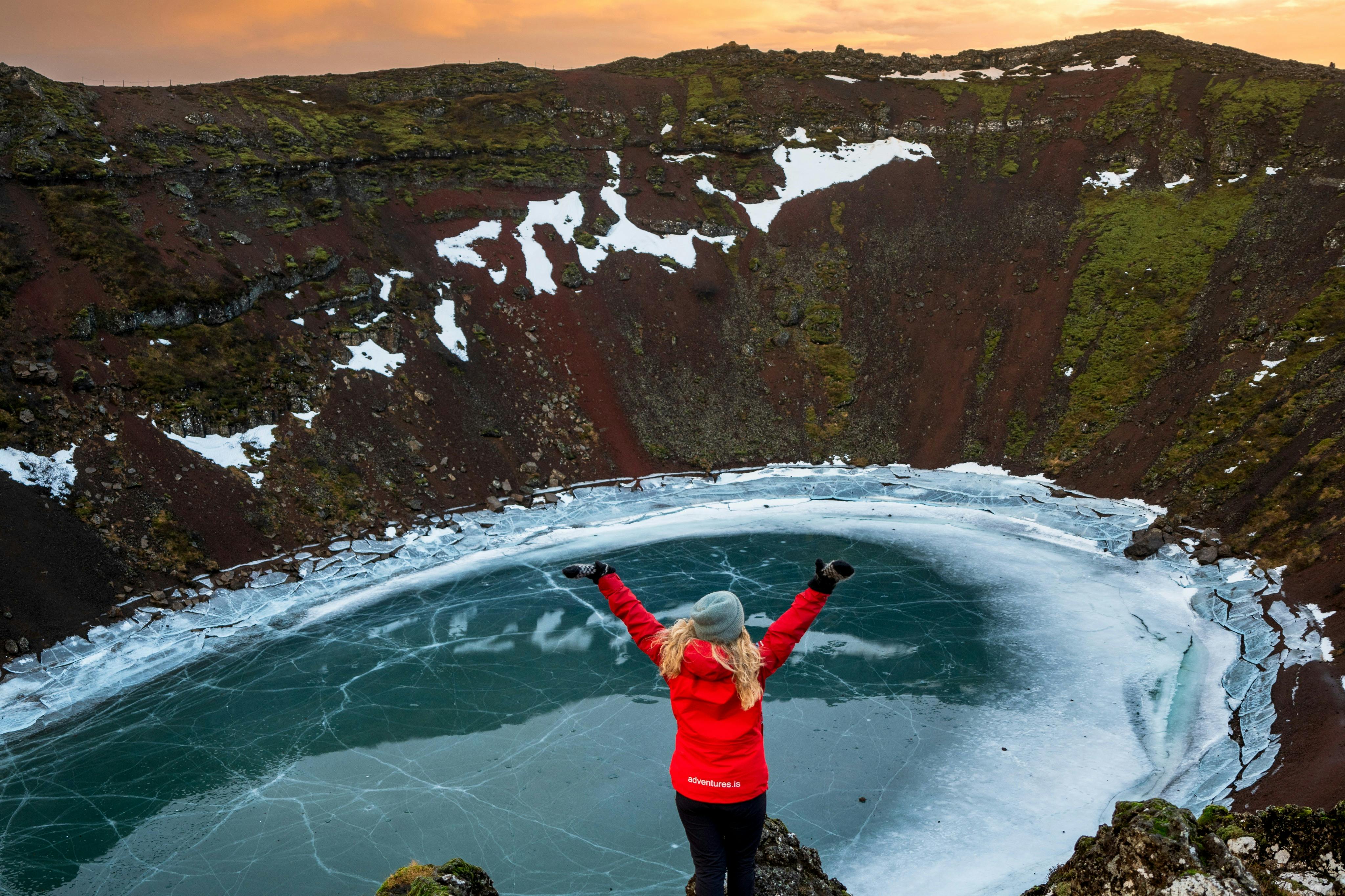 冬天，一个人站在岩石上俯瞰火山口。 湖水结冰了。