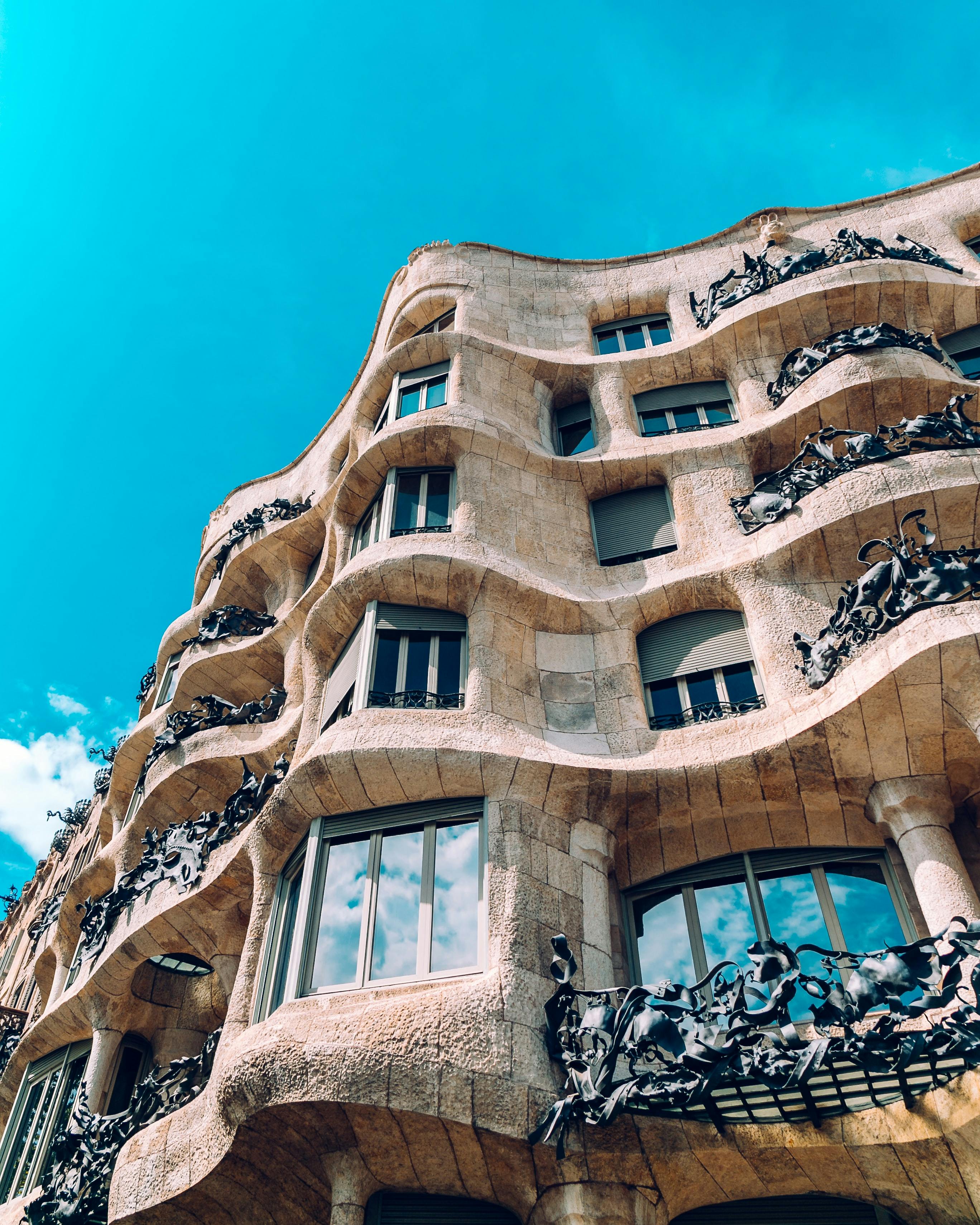 Curved, stone facade of a building with intricate wrought iron balconies, set against a bright blue sky.