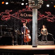 I musicisti si esibiscono sul palco con pianoforte, contrabbasso, bandoneon e violino. "El Querandí" è illuminato da luci rosse alle loro spalle.