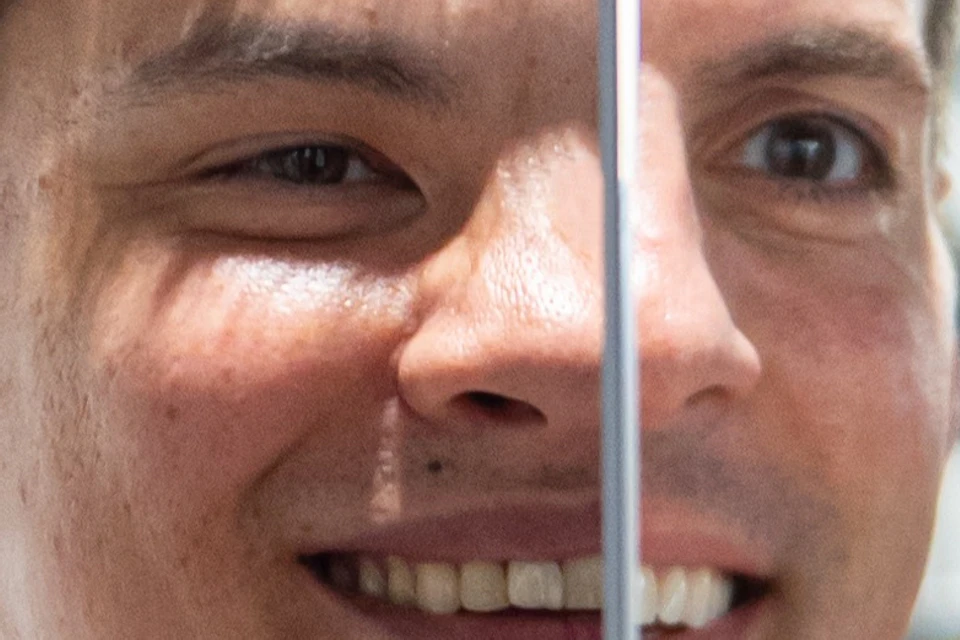 A person smiles while looking into a mirror, with their reflection visible. Blue geometric design in the background.