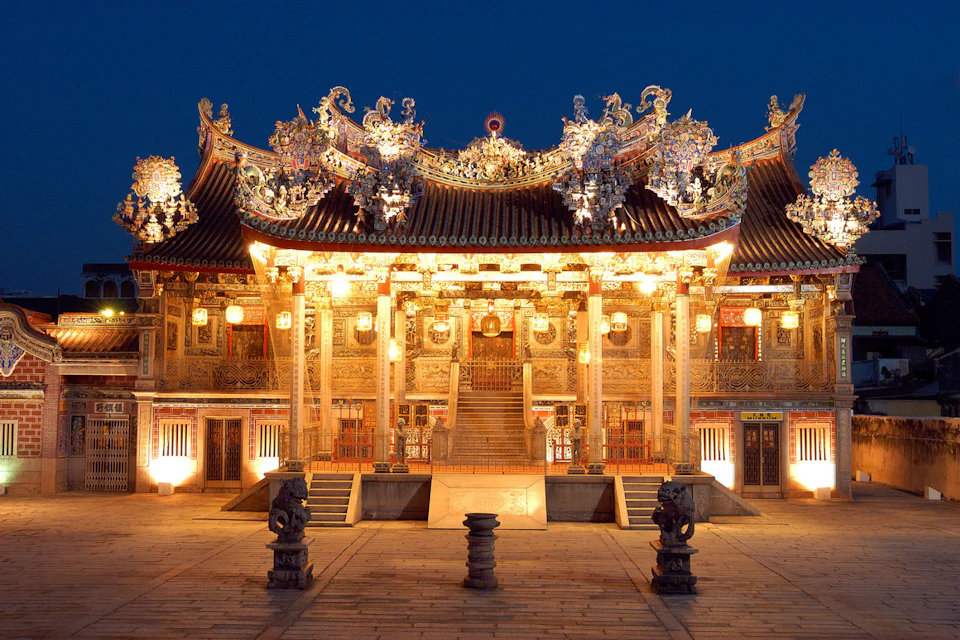 Ornate traditional Chinese temple lit up at night, featuring intricate carvings, lanterns, and a central staircase.