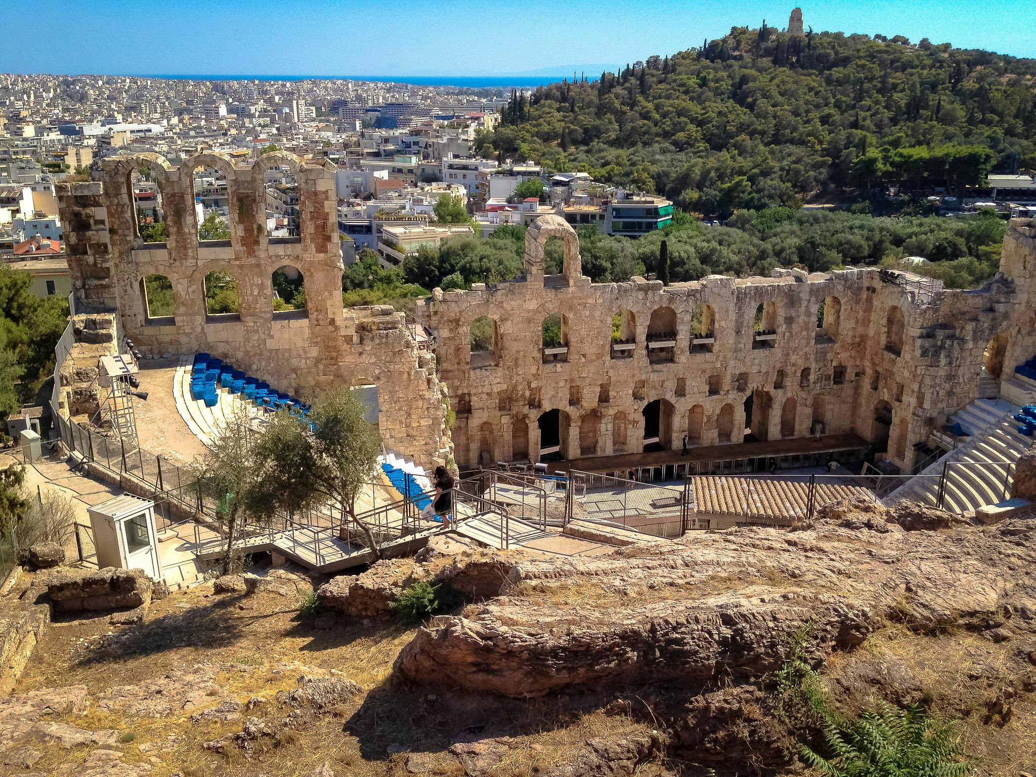 En gammal amfiteater i sten med nivåindelade sittplatser med utsikt över en stadsbild och omgiven av grönska på en sluttning.