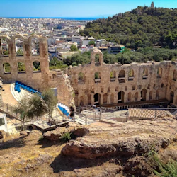 En gammal amfiteater i sten med nivåindelade sittplatser med utsikt över en stadsbild och omgiven av grönska på en sluttning.