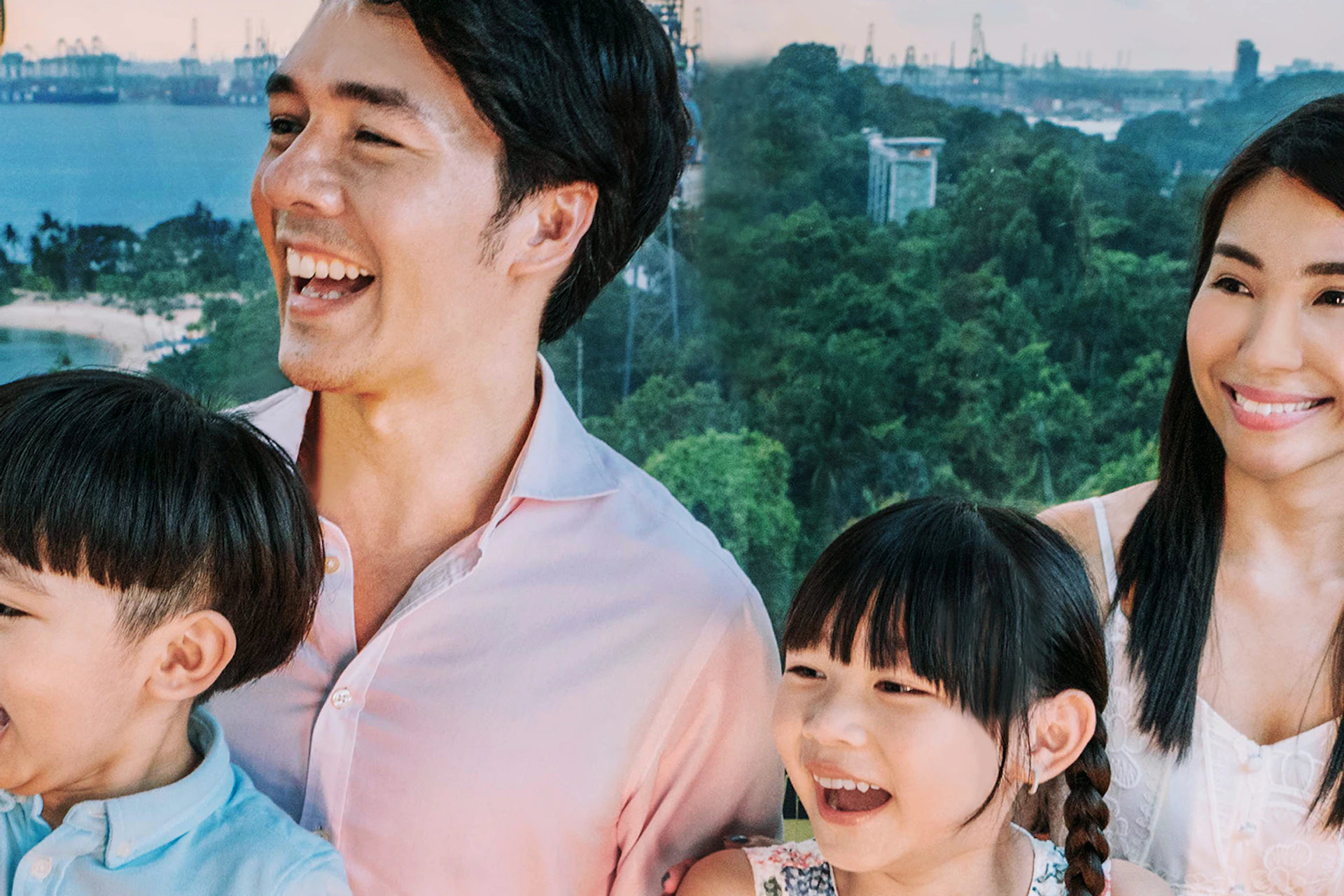 A family of four smiling and sitting inside a cable car with a scenic view of trees and coastline in the background.