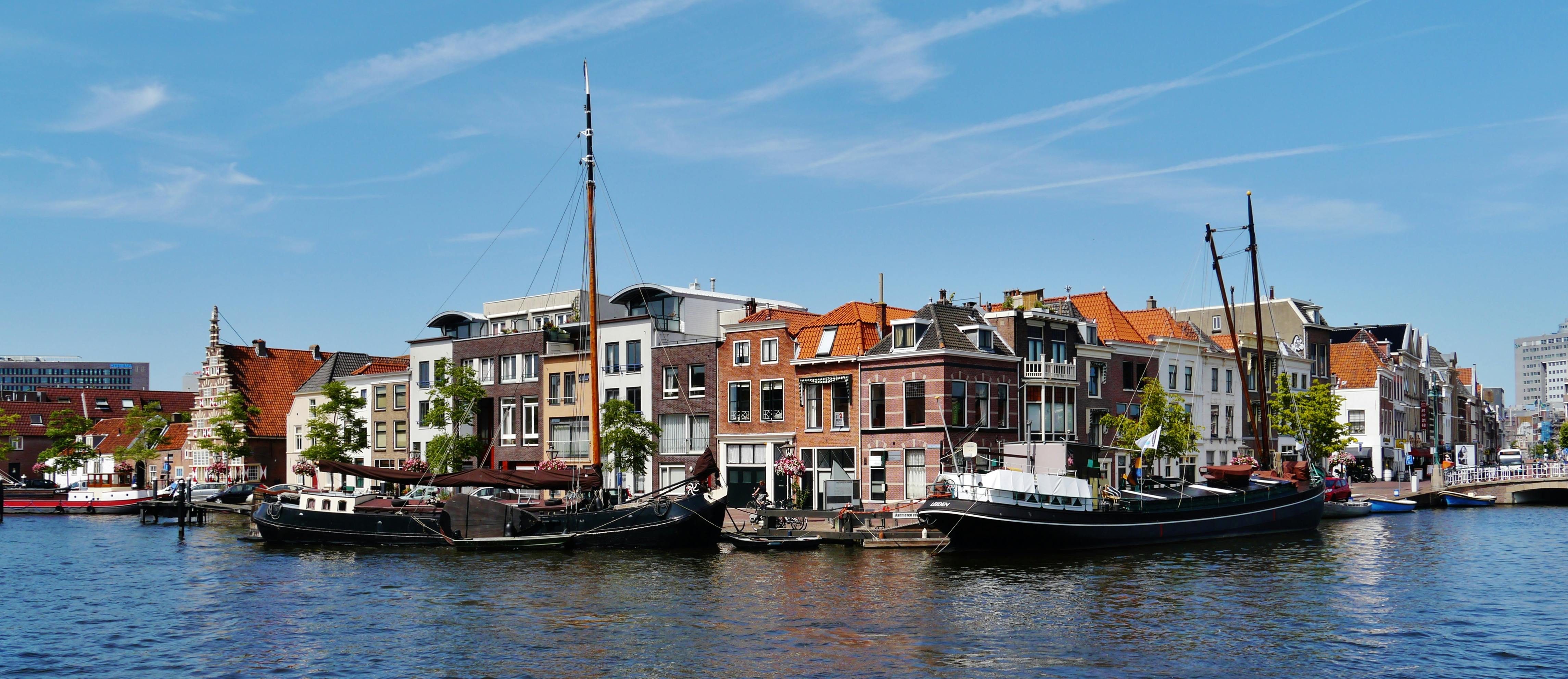 Kanál s ukotvenými plachetnicemi před řadou barevných budov pod jasně modrou oblohou.