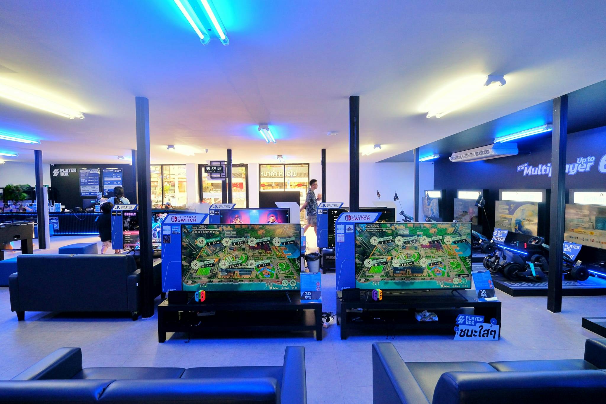 A brightly lit gaming center with multiple gaming stations, large screens, and players engaged in video games.