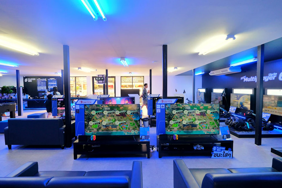 A brightly lit gaming center with multiple gaming stations, large screens, and players engaged in video games.