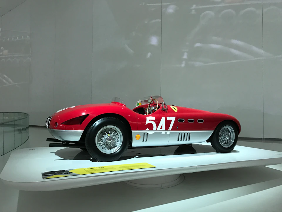 A vintage red and white race car with "547" on the side, displayed on a white platform in a museum-like setting.