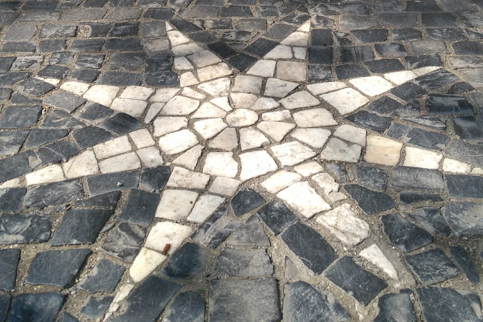 A mosaic star pattern made from white and dark stones on a cobblestone surface.