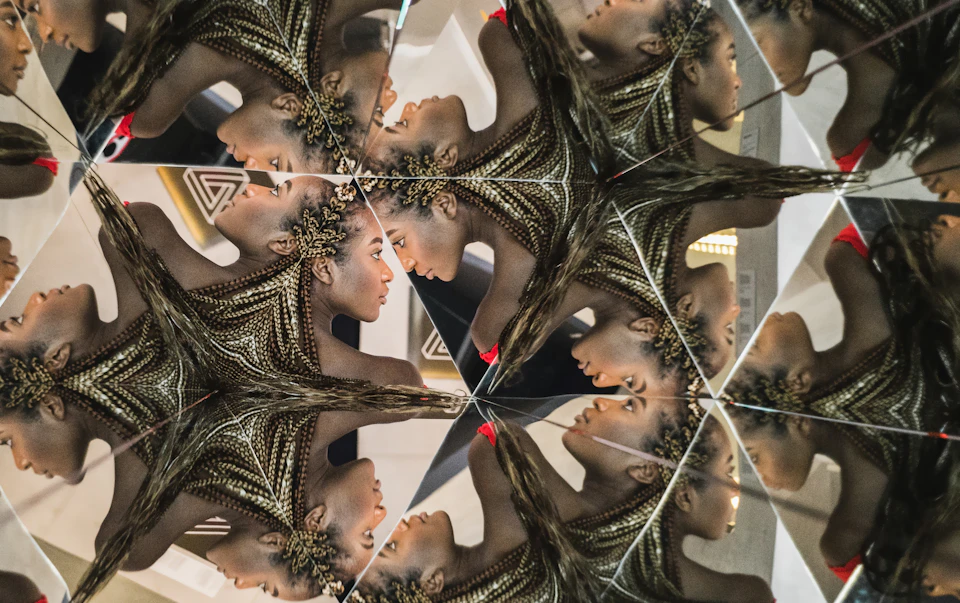 A kaleidoscopic image of a person with braided hair, showing multiple mirrored reflections of their head and shoulders.
