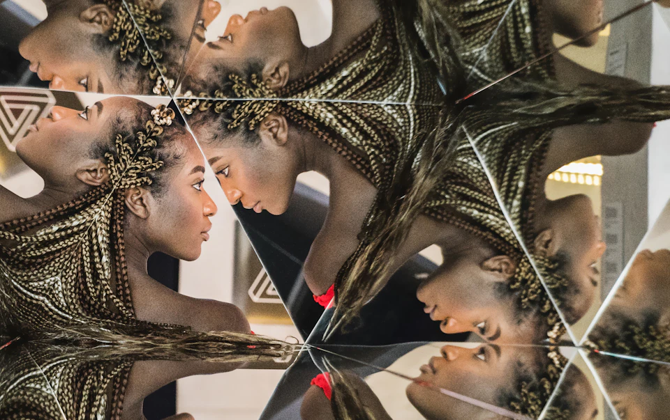A kaleidoscopic image of a person with braided hair, showing multiple mirrored reflections of their head and shoulders.