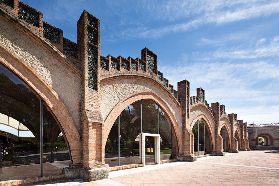 A building with a series of brick arches and large glass windows, featuring decorative elements under a blue sky.