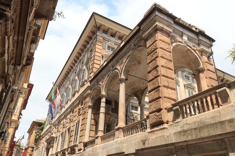 Large historic building with arched windows, ornate columns, and multiple flags displayed on the facade.