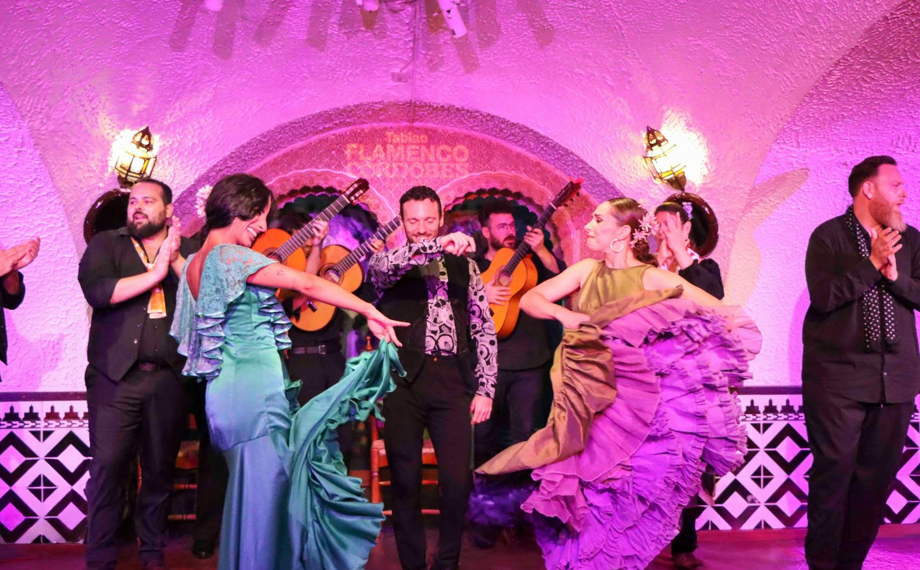 Spektakl flamenco z tancerzami i muzykami na scenie w fioletowym świetle.