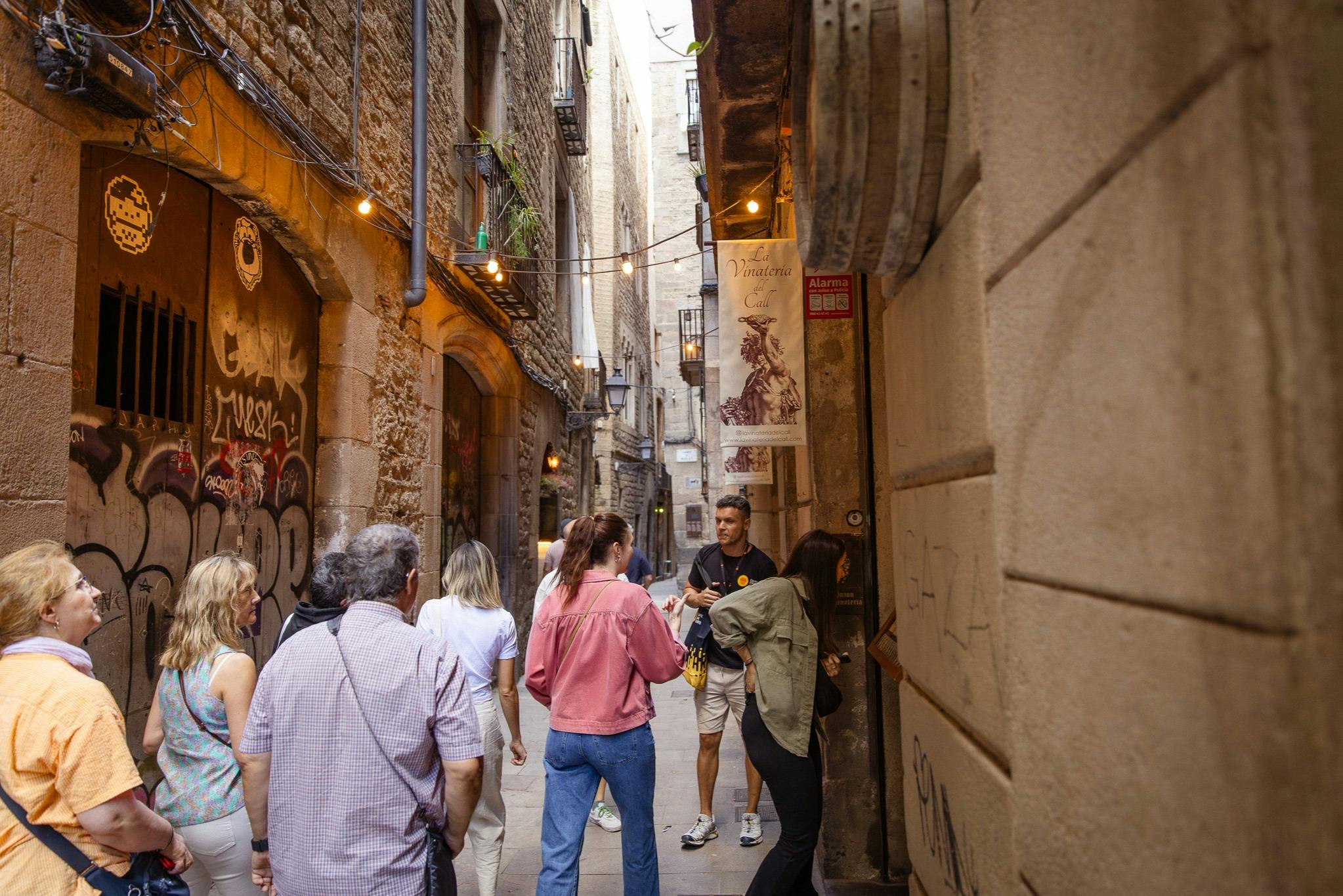 Un groupe de personnes marchant dans une ruelle historique étroite, ornée de graffitis et de guirlandes lumineuses dans un environnement urbain.