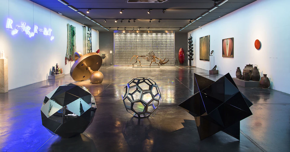 A modern art gallery with geometric sculptures, a rhino skeleton, various art pieces on the walls, and a polished concrete floor.