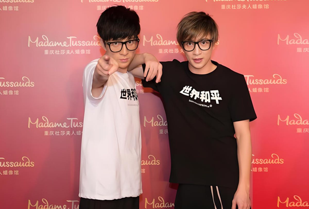 Dwie osoby w okularach i koszulkach tematycznych pozują na czerwonym tle z logo Madame Tussauds.