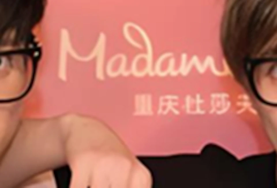 Two individuals wearing glasses and themed T-shirts pose in front of a red backdrop with the Madame Tussauds logo.