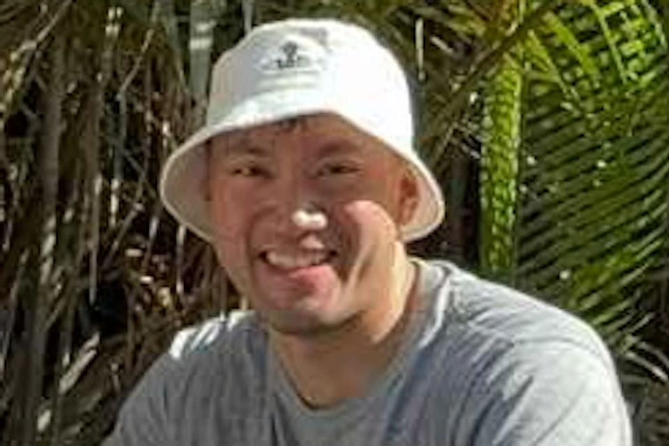 Four people in a wooden boat on a river, surrounded by lush tropical plants. They are smiling and wearing hats; one holds a camera.