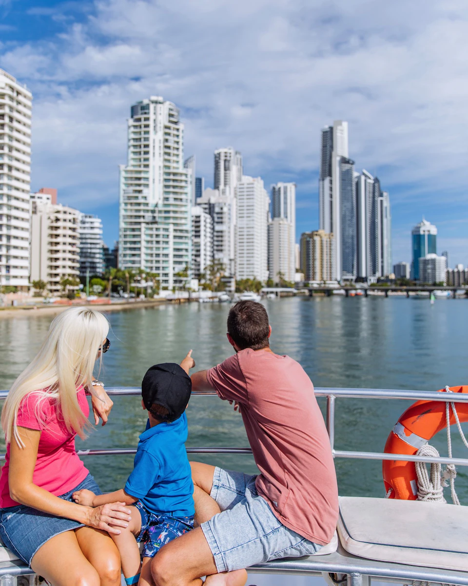 A woman, man, and child on a boat, looking at a city skyline with tall buildings across the water.