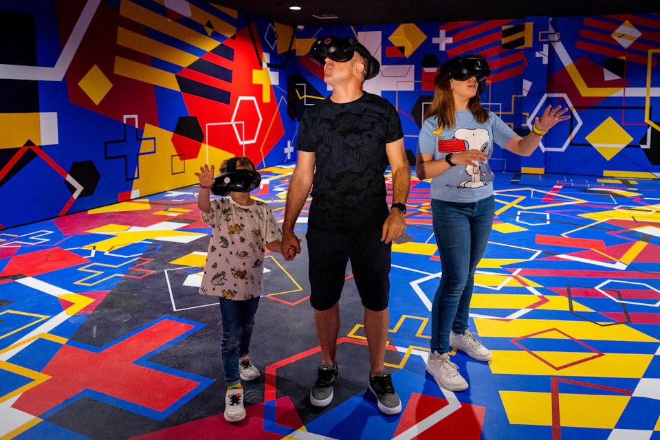 Three people wearing VR headsets in a colorful, patterned room with geometric designs on walls and floor.
