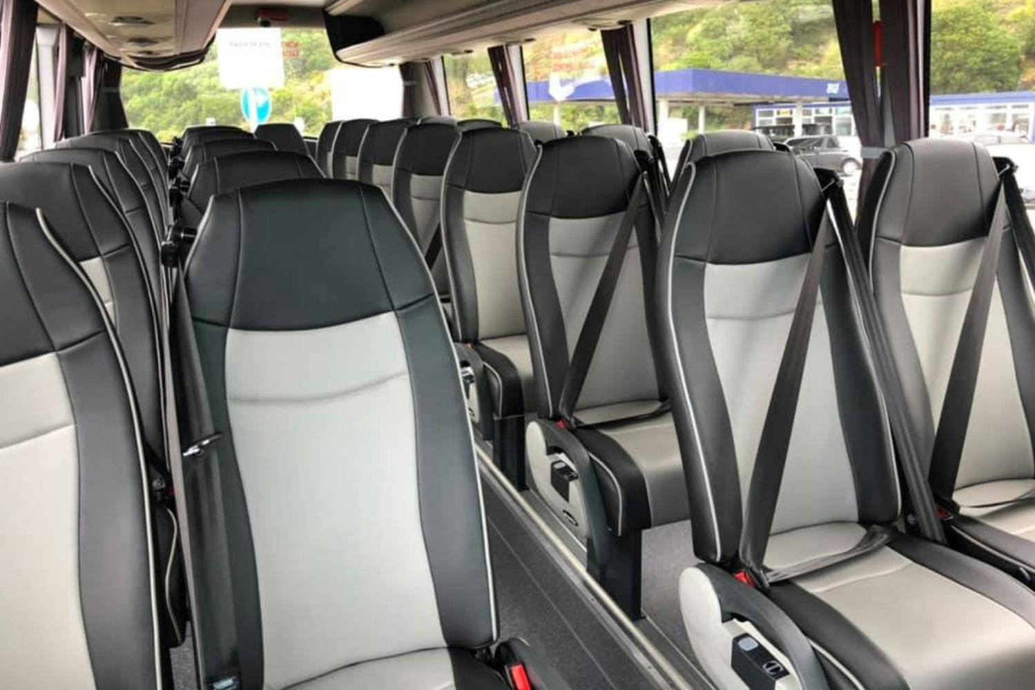 Interior of an empty bus with grey and black seats equipped with seat belts, viewed towards the front.