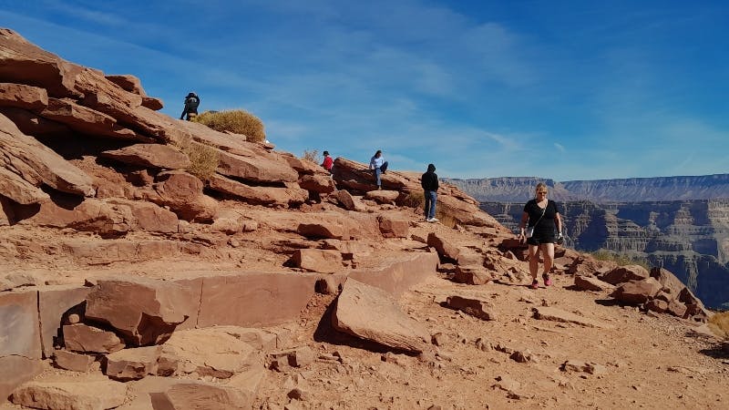 People hiking on a rocky terrain with brown large boulders and clear blue sky in the background.