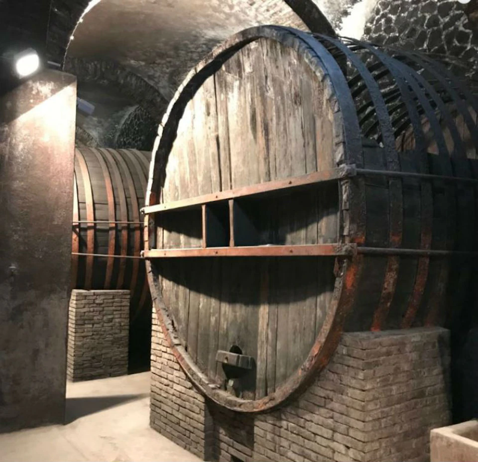 Large wooden barrels with metal bands and stone supports in a dimly lit cellar.
