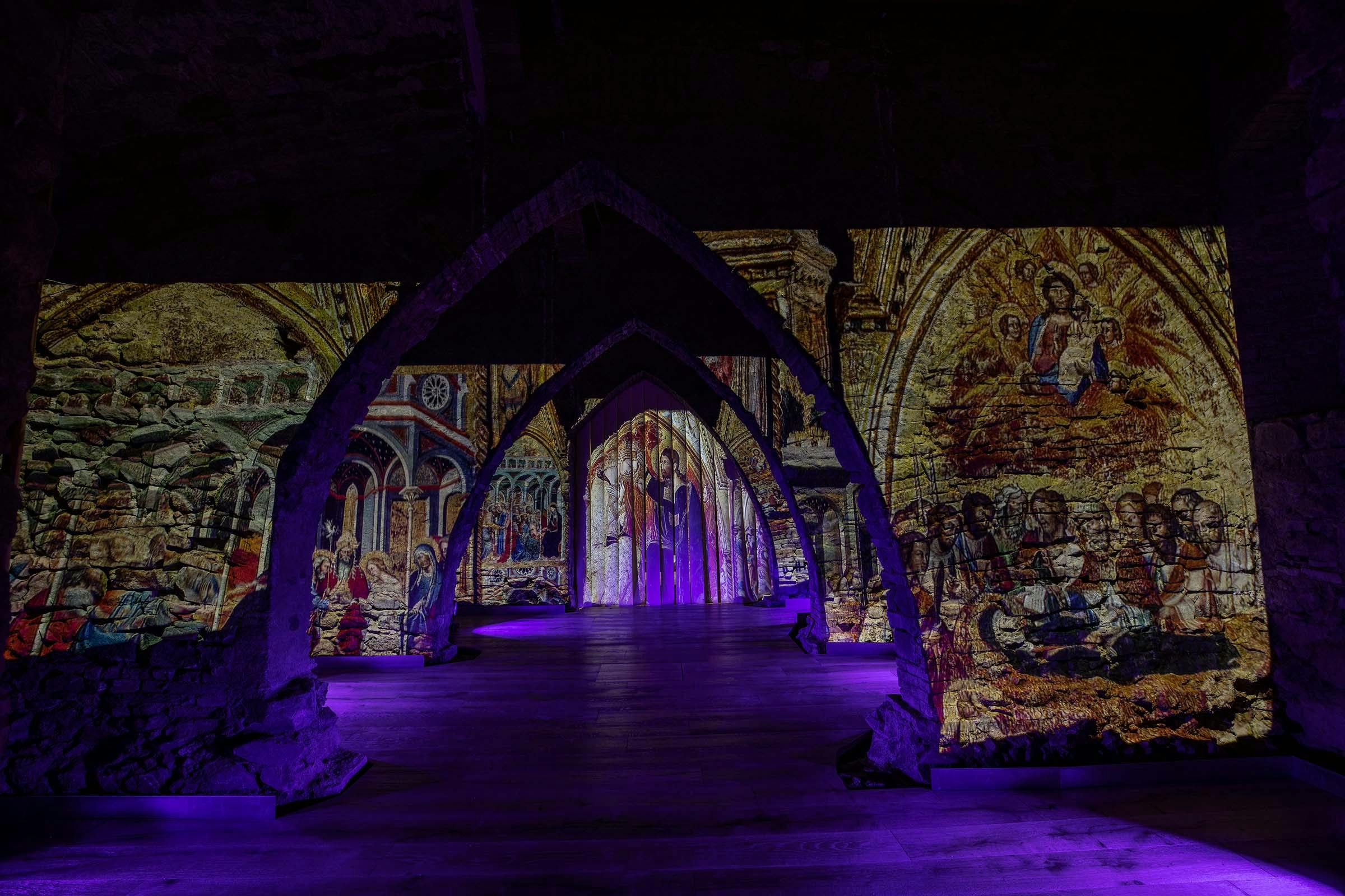 Arched stone structures with illuminated historical murals on walls, purple light accents, and wooden flooring.