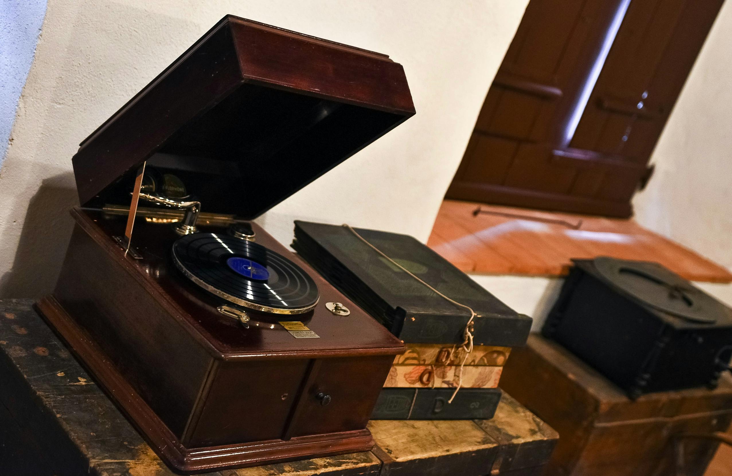 Vintage pladespiller med et åbent låg ved siden af en stak gamle bøger, placeret på en trækiste nær et vindue.